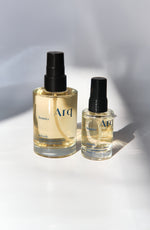Two glass bottles of Arq Botanics Refresh Hyaluronic Kakadu facial mist. The larger bottle has a pump dispenser, and the smaller one has a spray nozzle. Both are resting on a white surface.