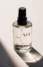 A glass bottle of Arq Botanics Glow Rose Botanical Facial Mist with a black spray pump, sitting on a white surface.